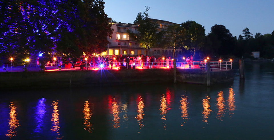 Beleuchtetes Seeufer mit stehenden Menschen an der Lindauer Nobelpreisträgertagung